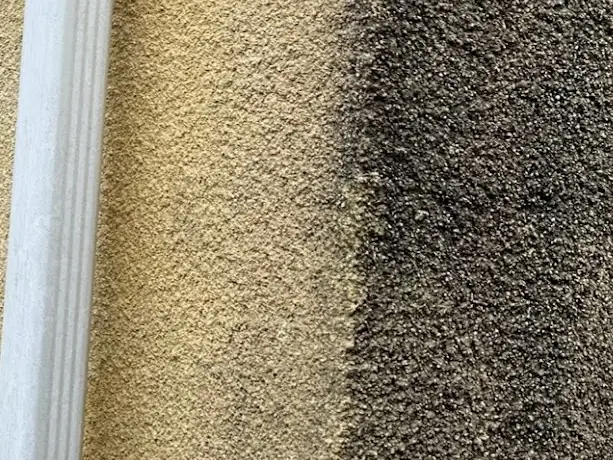 Façade en crépi jaune en cours de nettoyage, à côté d'une descente d'eau : à gauche la partie nettoyée, à droite le crépi encore noir